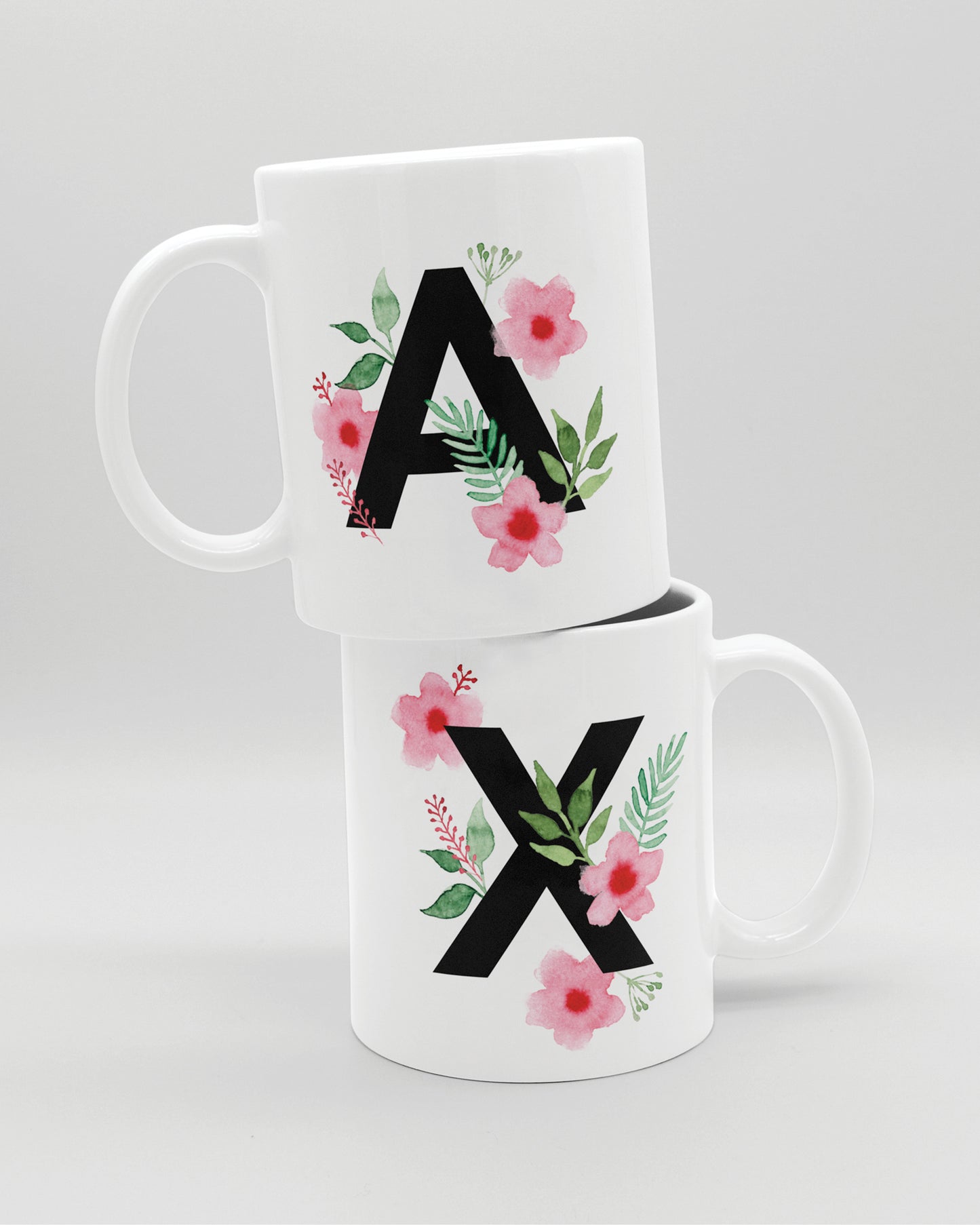 Zwei weiße Keramiktasse aufeinander, mit schwarzem Buchstaben A und X und rosa-grünen Aquarell-Blumen
