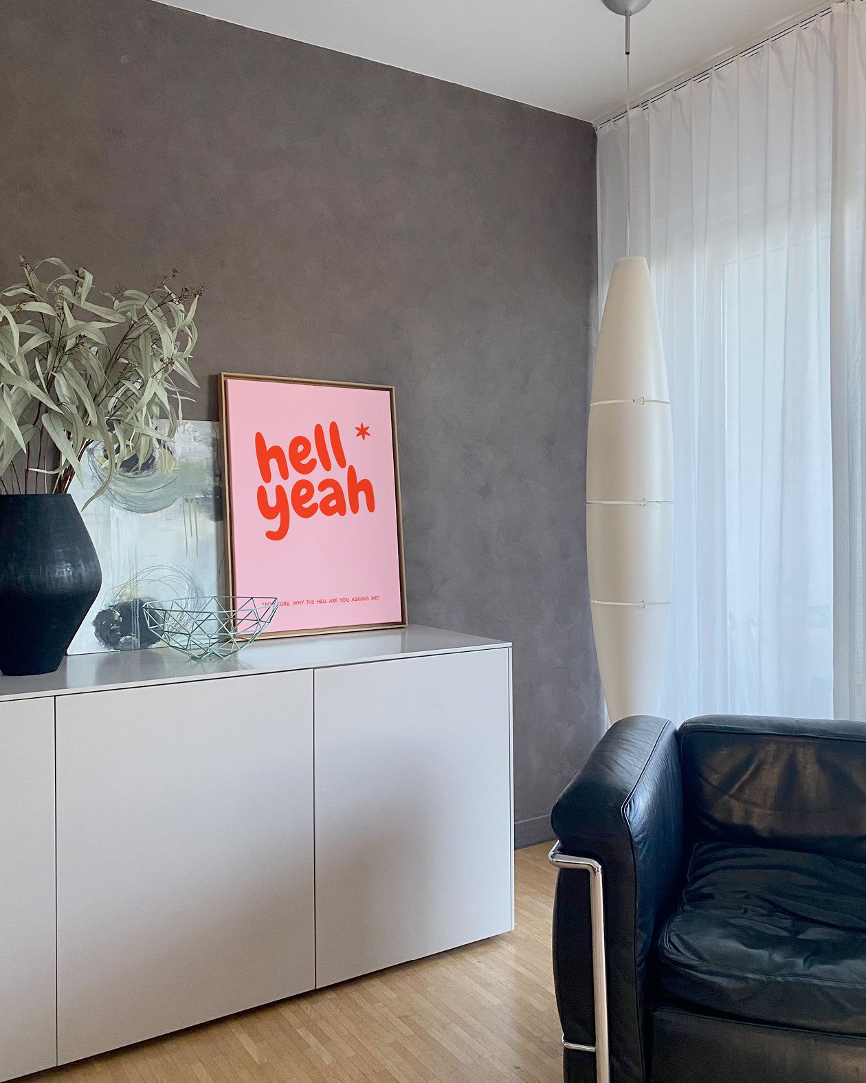 Leinwandbild „Hell Yeah" im Eichen-Schattenfugenrahmen auf Sideboard, im Hintergrund Vorhang, Ledersessel und Deckenlampe.