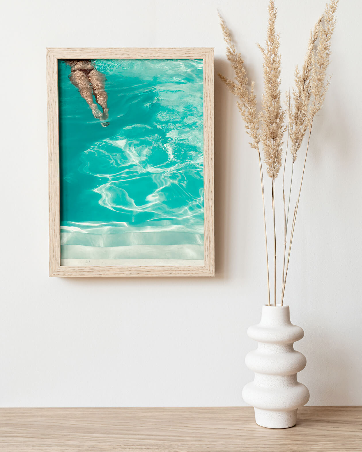 Poster The Pool Girl in einem Holzrahmen über einem Regal mit Vase. Fotografie mit türkisfarbener Wellenstruktur und Beine einer Frau im Anschnitt, moderne Wandkunst.