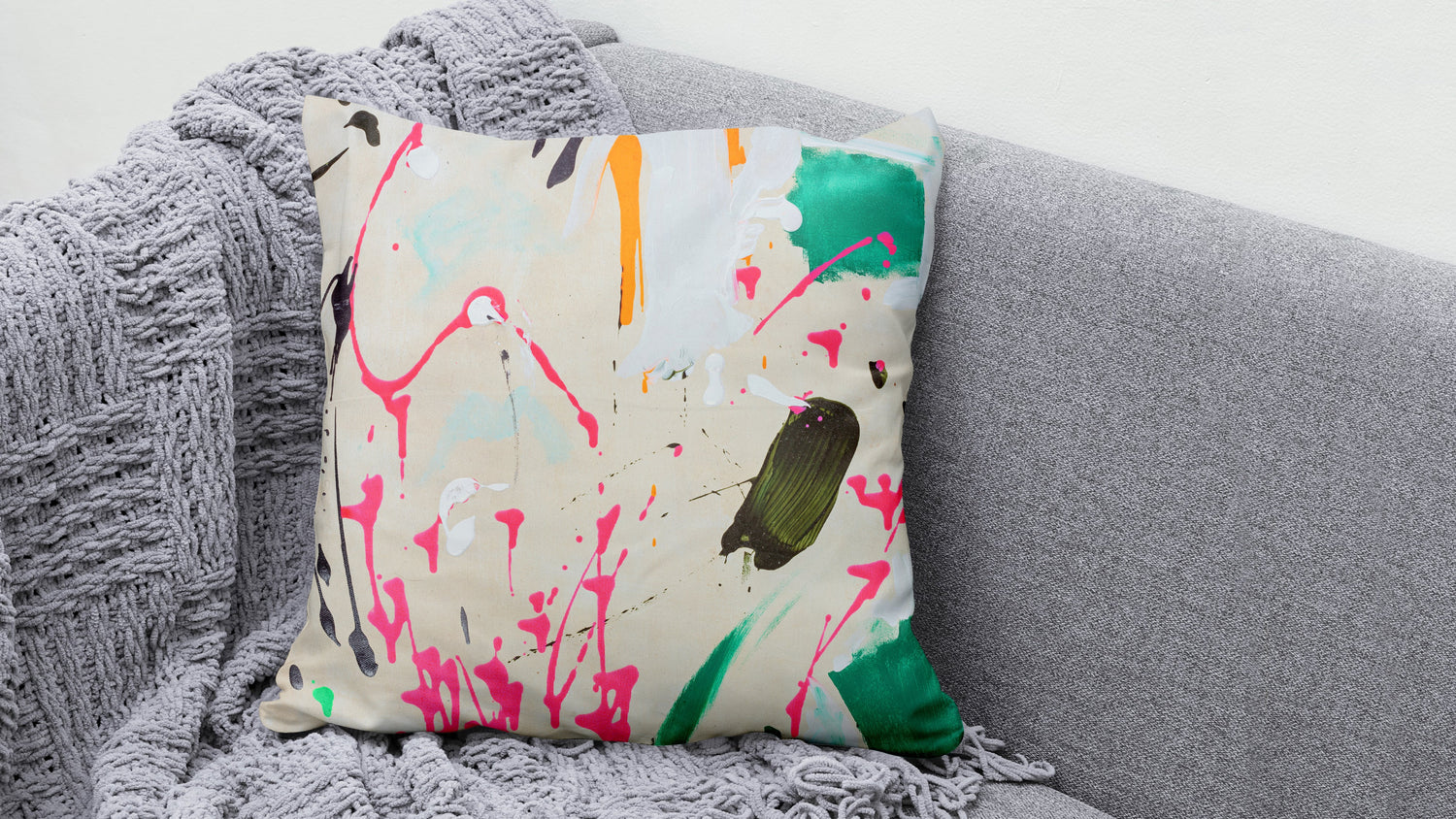 Kissen mit Farbspritzer "Drip Happens" auf einem grauen Sofa