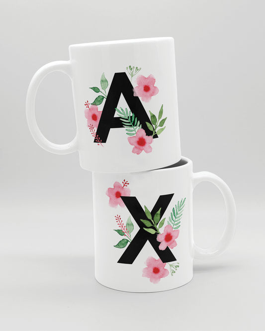 Zwei weiße Keramiktasse aufeinander,  mit schwarzem Buchstaben A und X und rosa-grünen Aquarell-Blumen