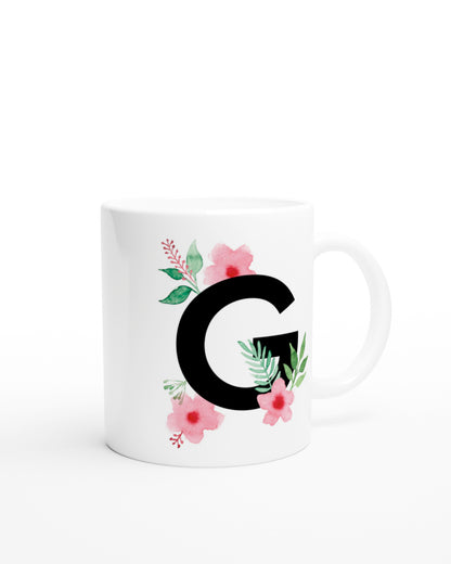 Weiße Keramiktasse mit schwarzem Buchstaben G und rosa-grünen Aquarell-Blumen