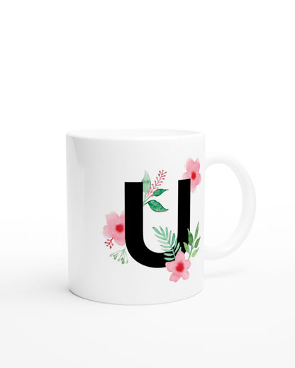 Weiße Keramiktasse mit schwarzem Buchstaben U und rosa-grünen Aquarell-Blumen