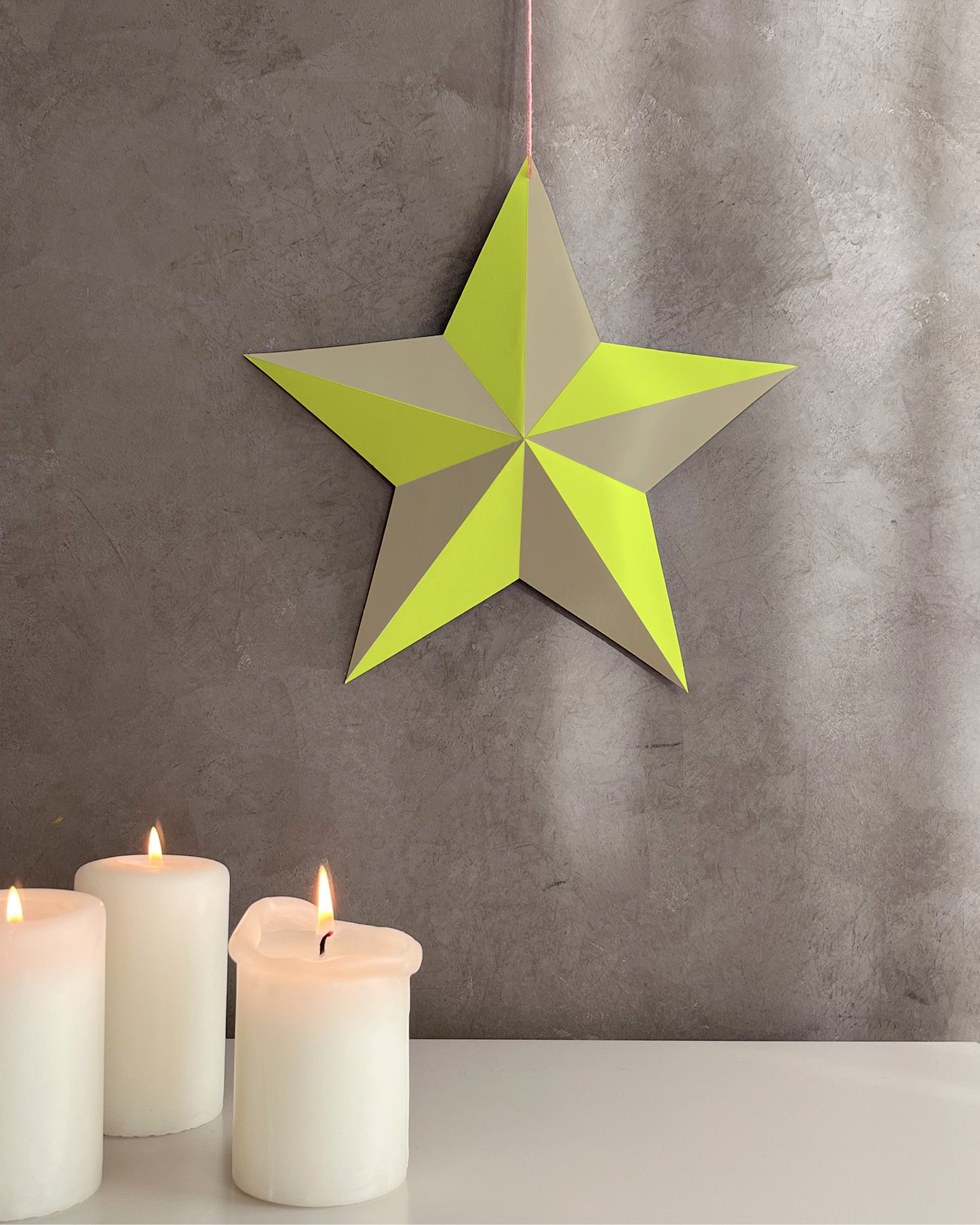 Fertig gebastelter, dekorativer Stern in Neon-Gelb und Sandbeige vor grauer Wand, im modernen Interior