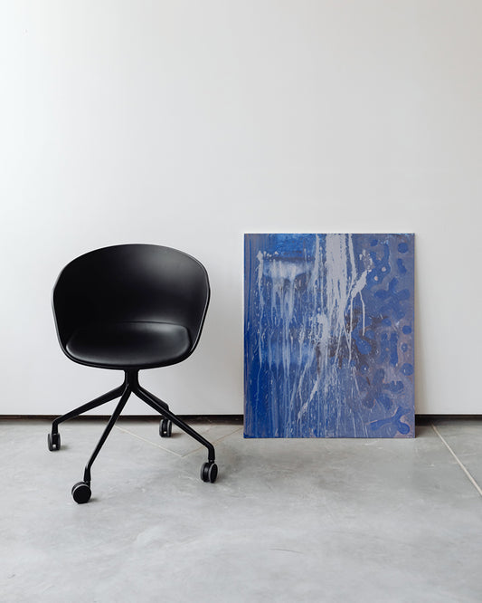 Das Bild "Blue Abstract" lehnt neben einem modernen Bürostuhl an der Wand.
