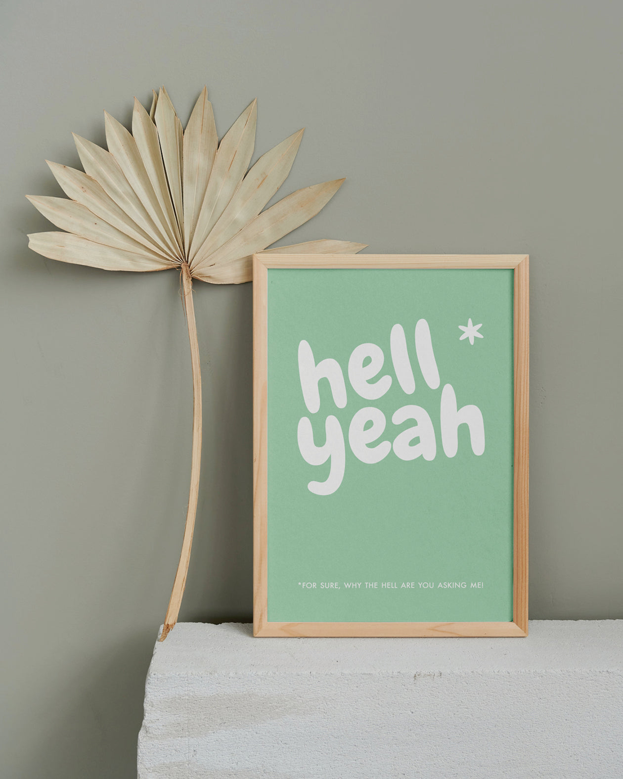 Poster "Hell Yeah" in Holzrahmen auf einem Steinsims mit Blattdeco.
