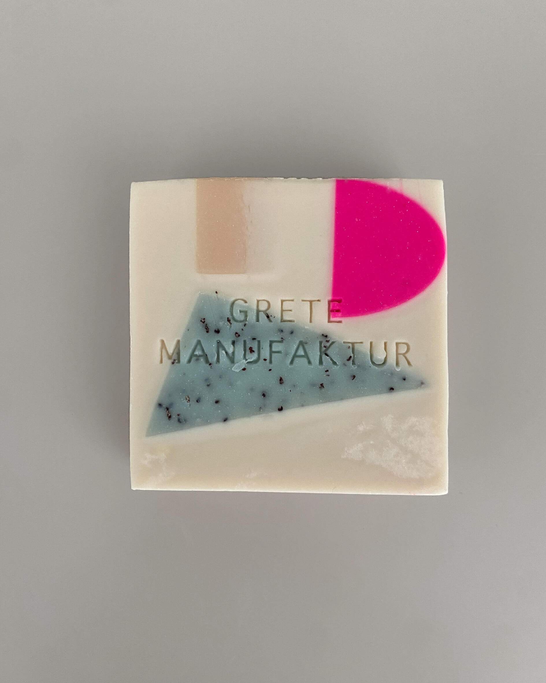 Seifenstück Constanze in Off-White mit geometrischen Einschlüssen in Neonpink, Hellblau mit Sprenkeln und Beige. 