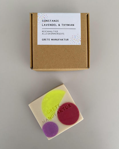 Buntes Seifenstück liegt neben einer Verpackung aus Naturpappe.