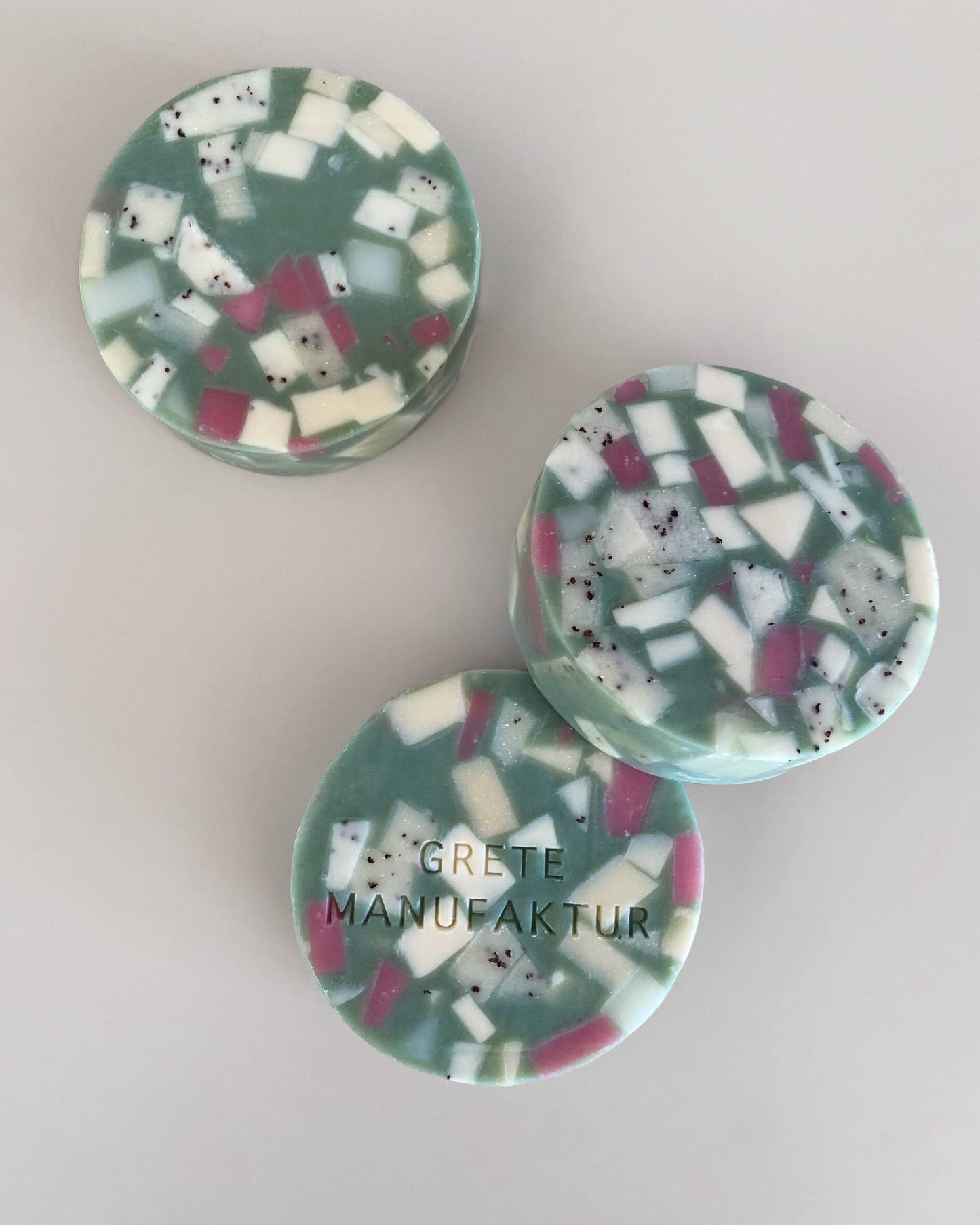 Drei runde Ette Seifen im Terrazzo-Design. Türkis mit geometrischen Fragmenten in Weiß und Lila.