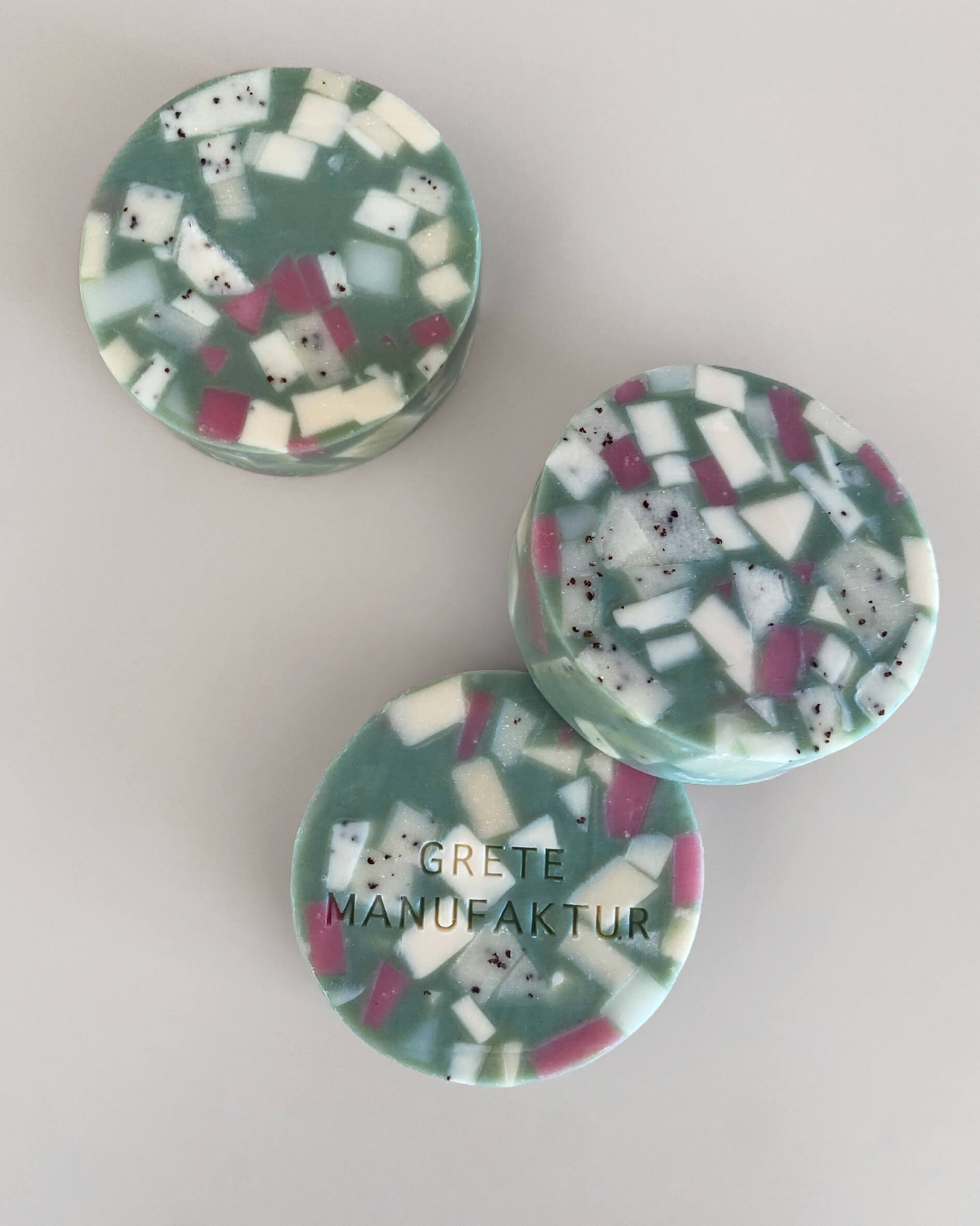 Drei runde Ette Seifen im Terrazzo-Design. Türkis mit geometrischen Fragmenten in Weiß und Lila.