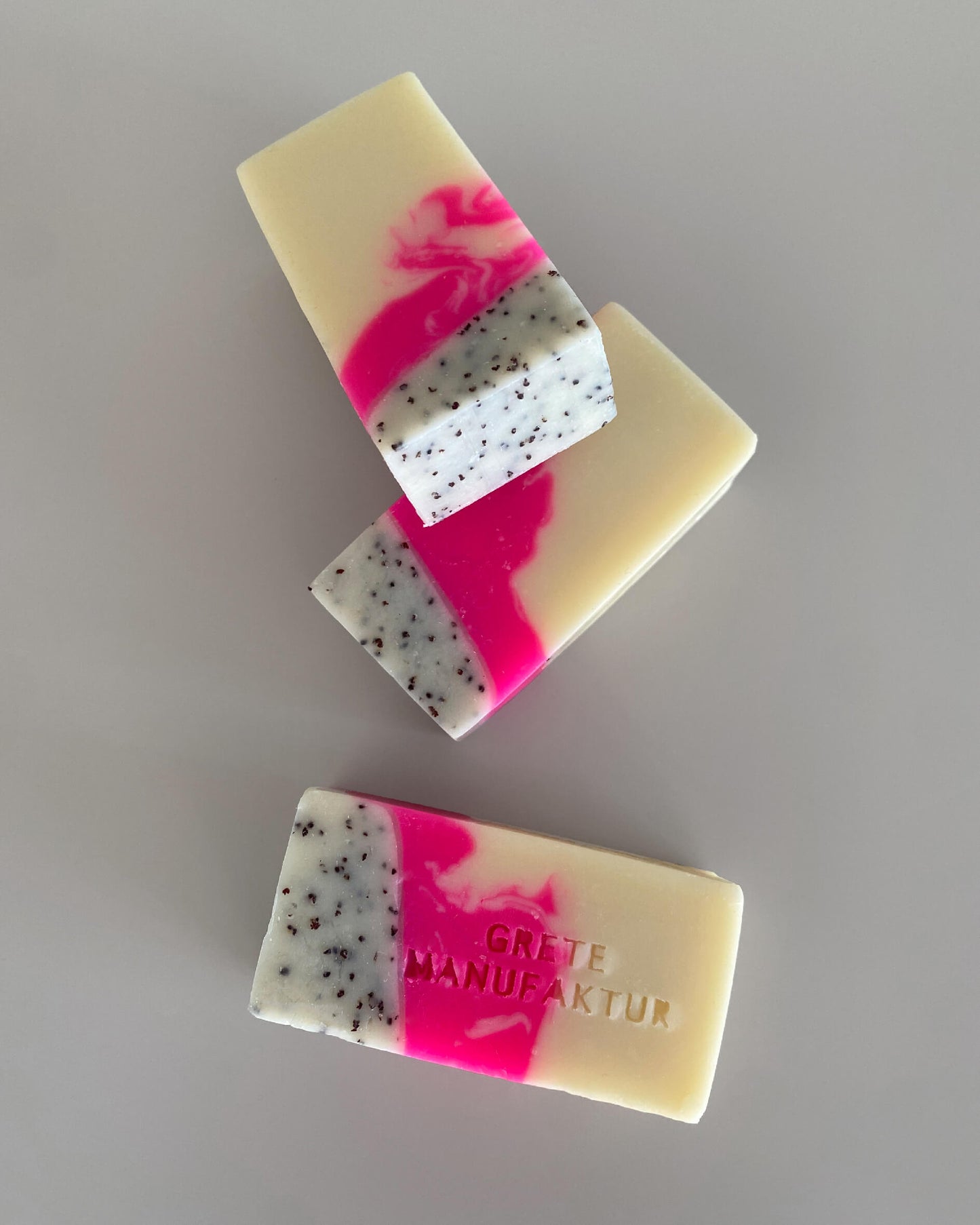 Drei Seifenstücke mit hochwertig handgemachter Haptik und einer dreifachen Farbgebung: Neonpink, Creme und schwarz gesprenkelt. Mit Buchstabenprägung auf einer Seife: Grete Manufaktur
