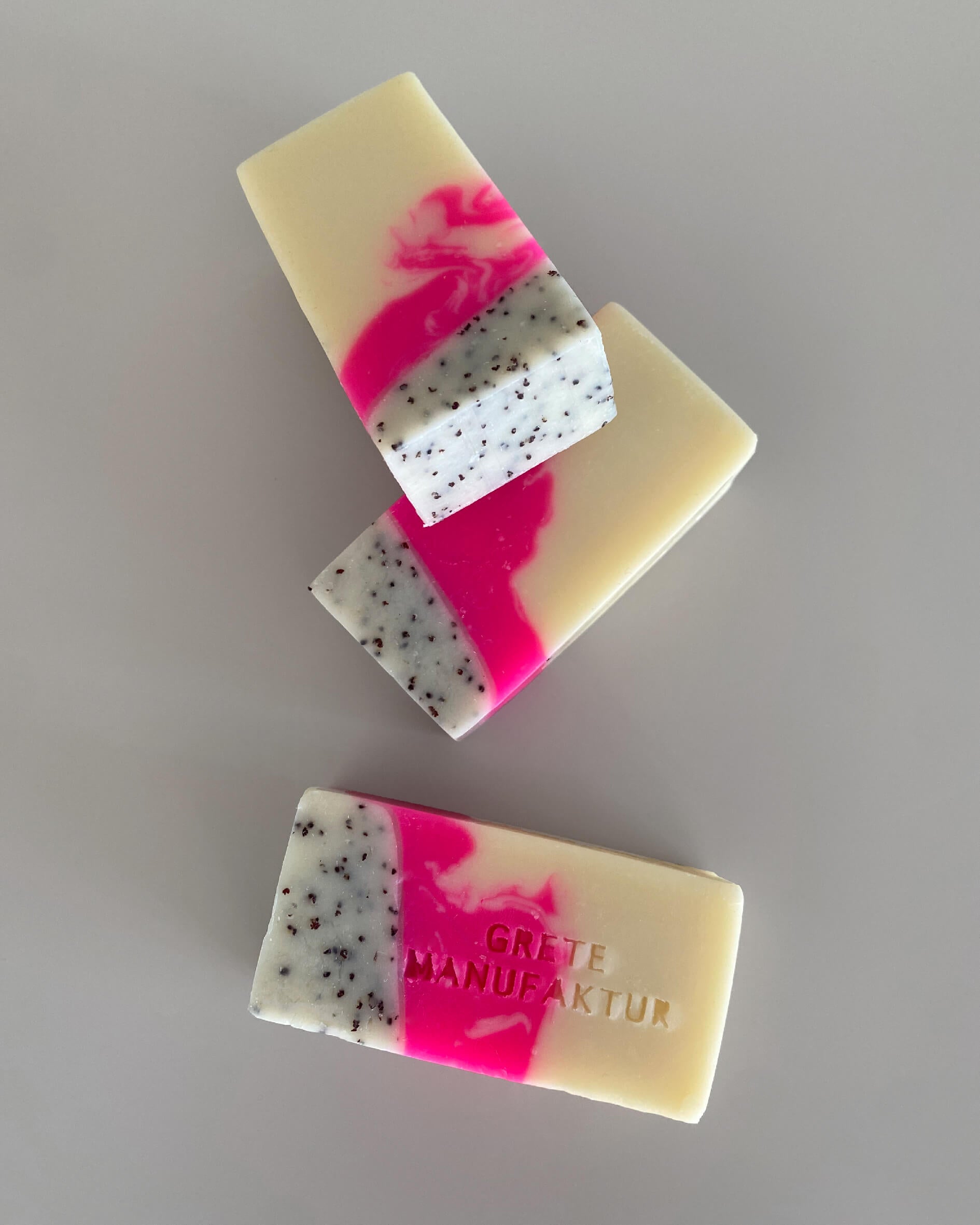 Drei Seifenstücke mit hochwertig handgemachter Haptik und einer dreifachen Farbgebung: Neonpink, Creme und schwarz gesprenkelt. Mit Buchstabenprägung auf einer Seife: Grete Manufaktur