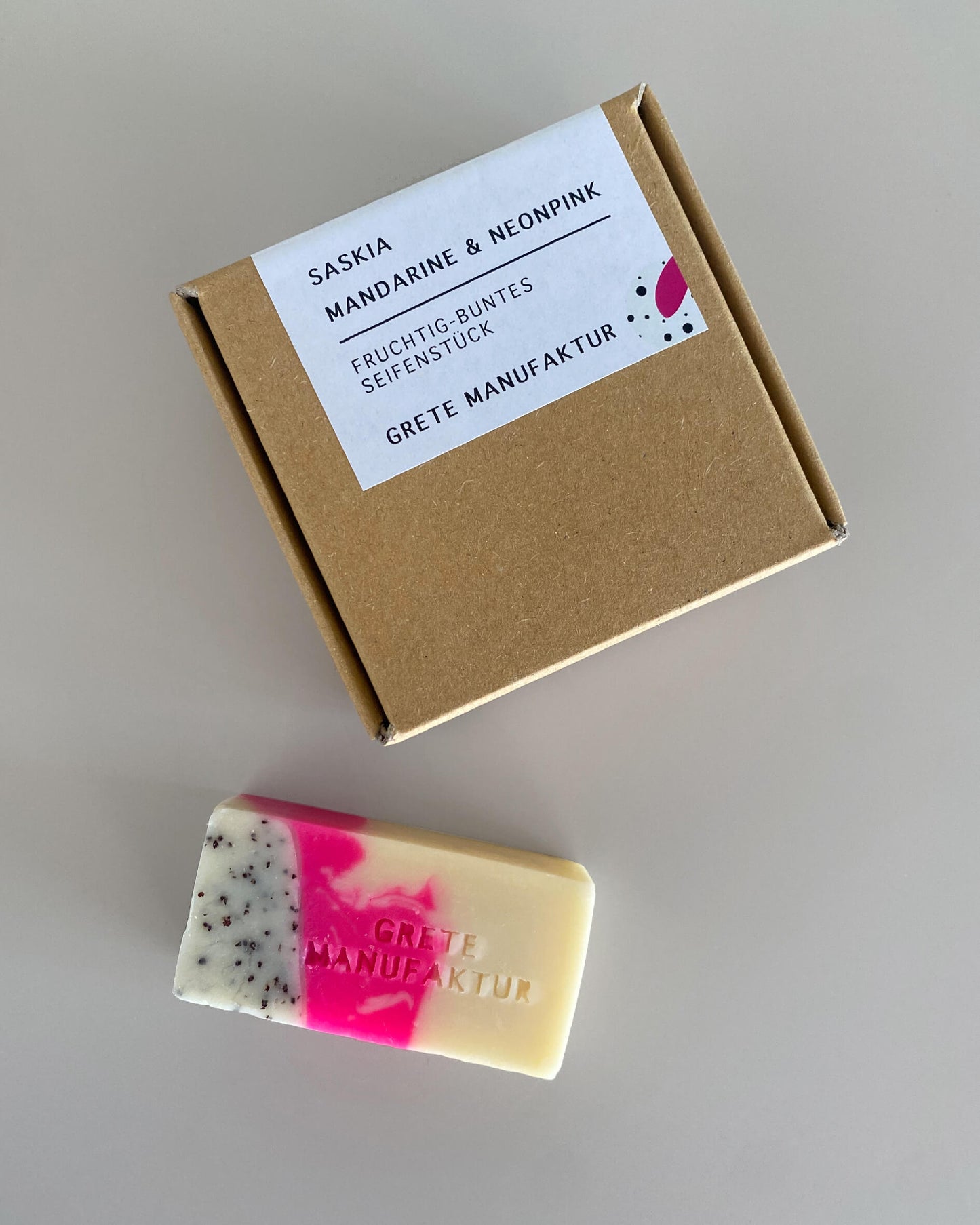 Seifenstück "Saskia" liegt neben der Verpackung auf grauem Hintergrund