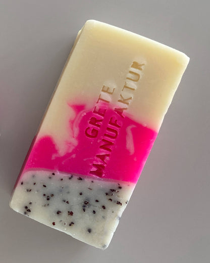 Nahaufnahme einer Seife mit hochwertig, handgemachter sichtbarer Oberfläche mit auffälliger Farbkombination: Cremefarben, Neonpink und ein Teil Weiss mit schwarzer Peelingstrucktur. 