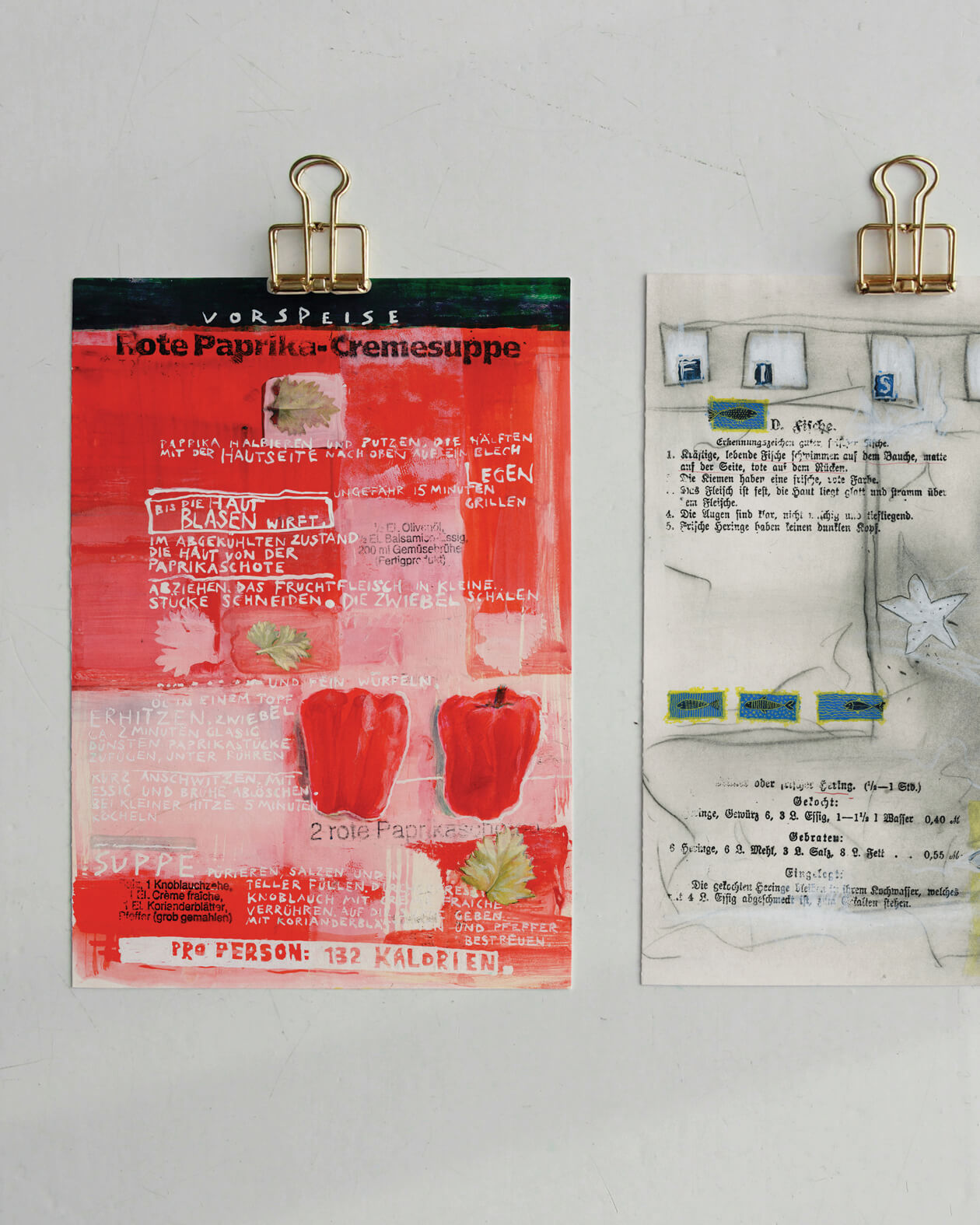 Zwei Poster vor grauem Hintergrund mit Klammern fixiert. Links sieht man das Poster Rote Paprika-Cremesuppe von Myria Notarnicola, rechts einen Teil des Posters Fisch.